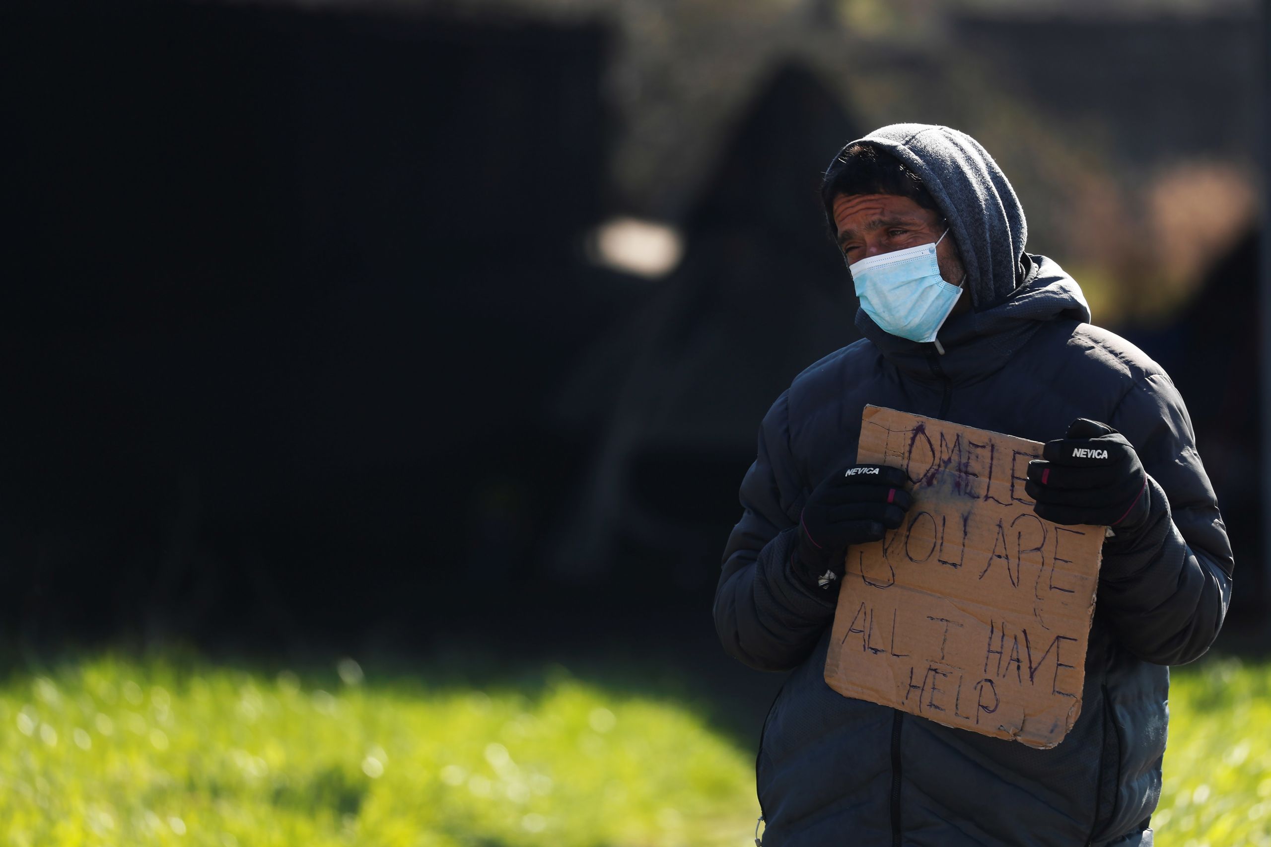 Obdachloser mit Mund- und Nasenschutzmaske hält Pappschild hoch auf dem steht: Homeless. You are all I have. Help!