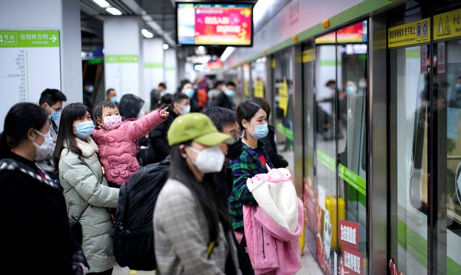 Foto einer Chinesischen Bahn-Station. Menschen mit Masken stehen vor einem Wagon.