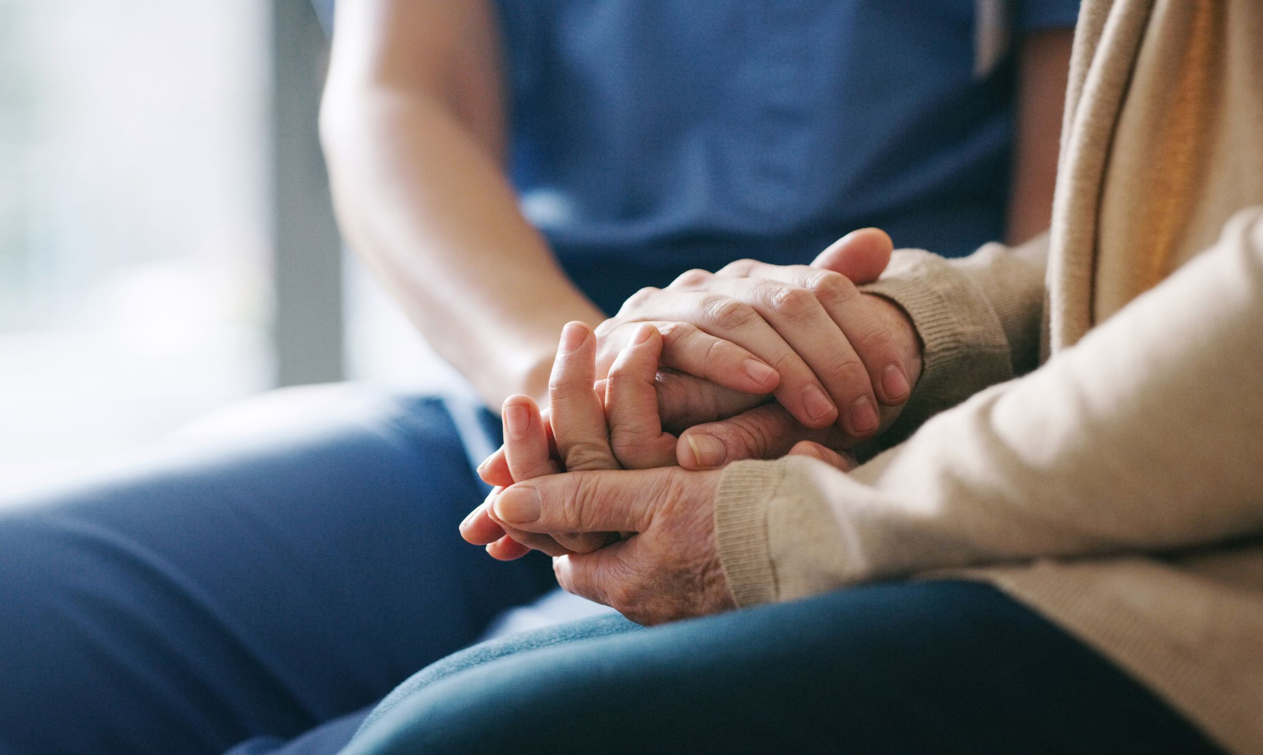 Das Bild zeigt die Hand einer Pflegekraft, die auf der Hand eines älteren Menschen liegt