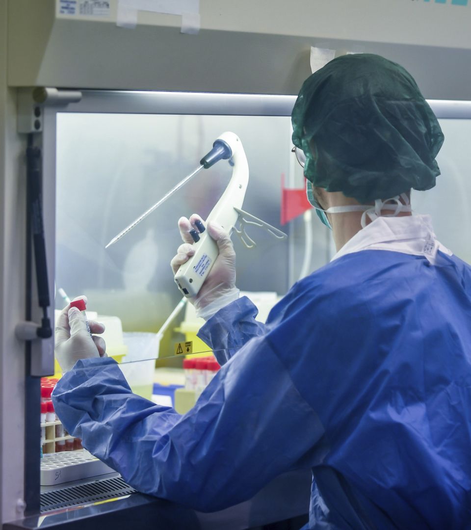 Mann in Schutzkleidung untersucht Probe im Labor